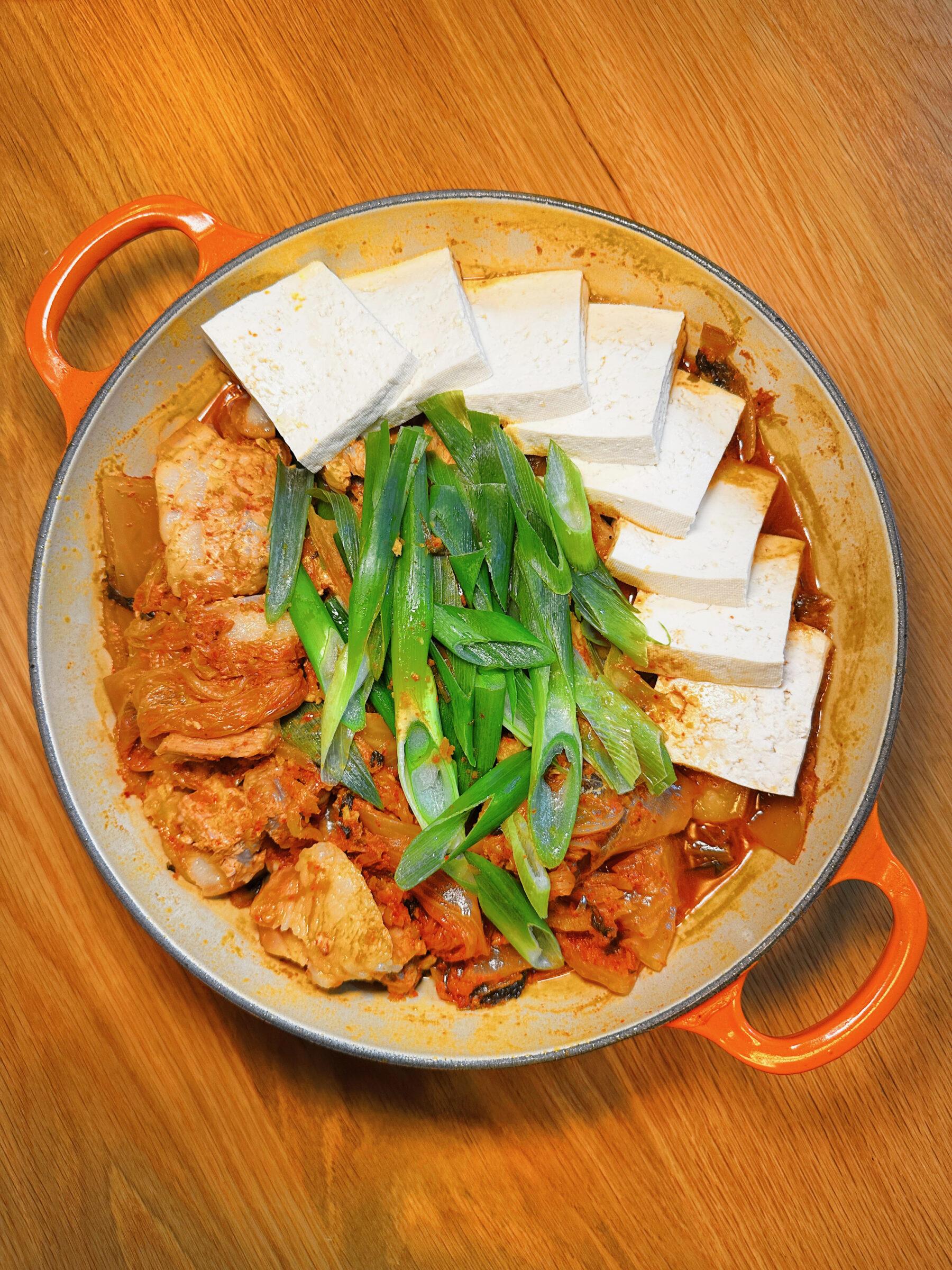 Kimchi-braised pork belly with tofu and green onions arranged in a round dutch oven, ready to serve.