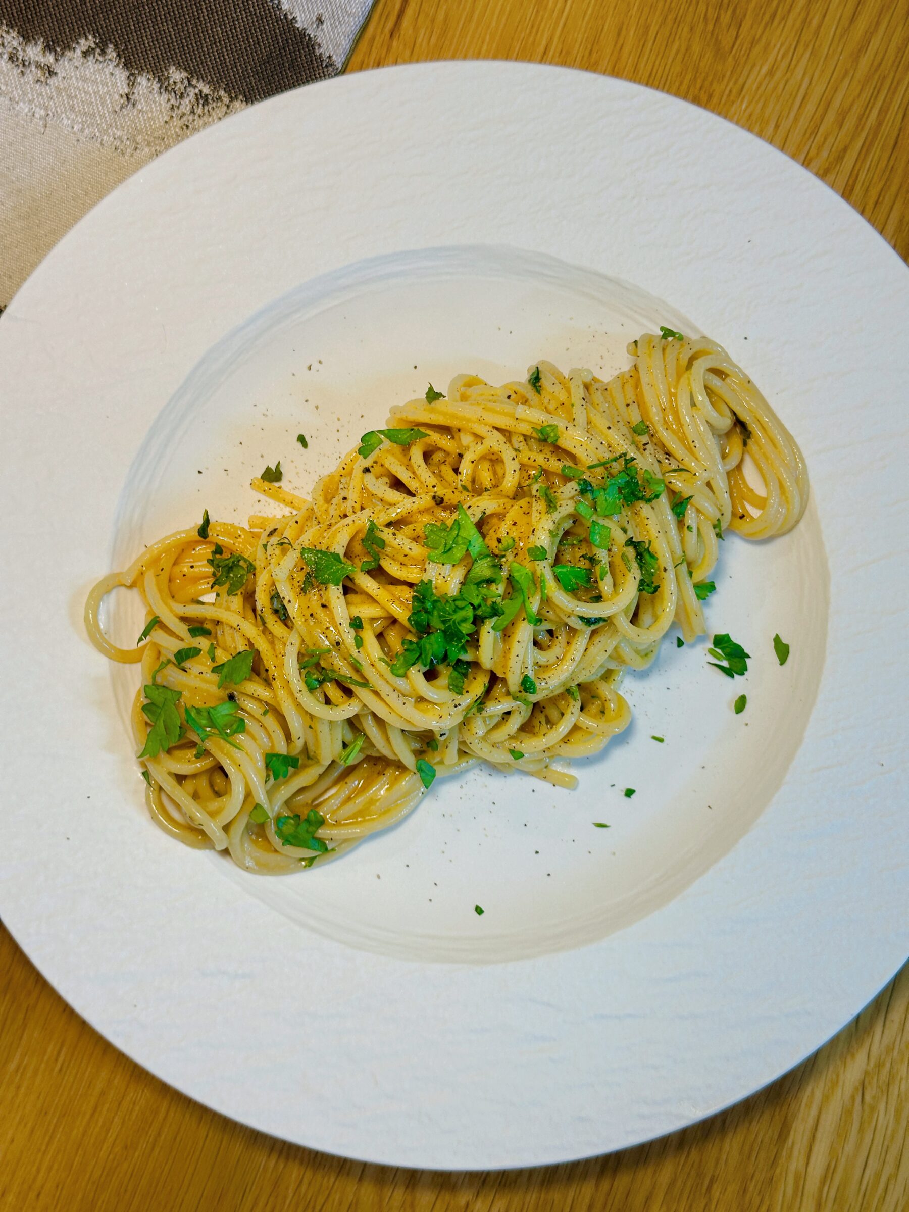 Anchovy lemon butter spaghetti served on a white plate with chopped parsley and black pepper on top