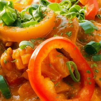 Close-up of rose chicken in creamy tomato sauce with red and yellow bell peppers and green onions
