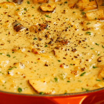 Creamy mushroom sauce simmering in an orange pot with herbs and black pepper