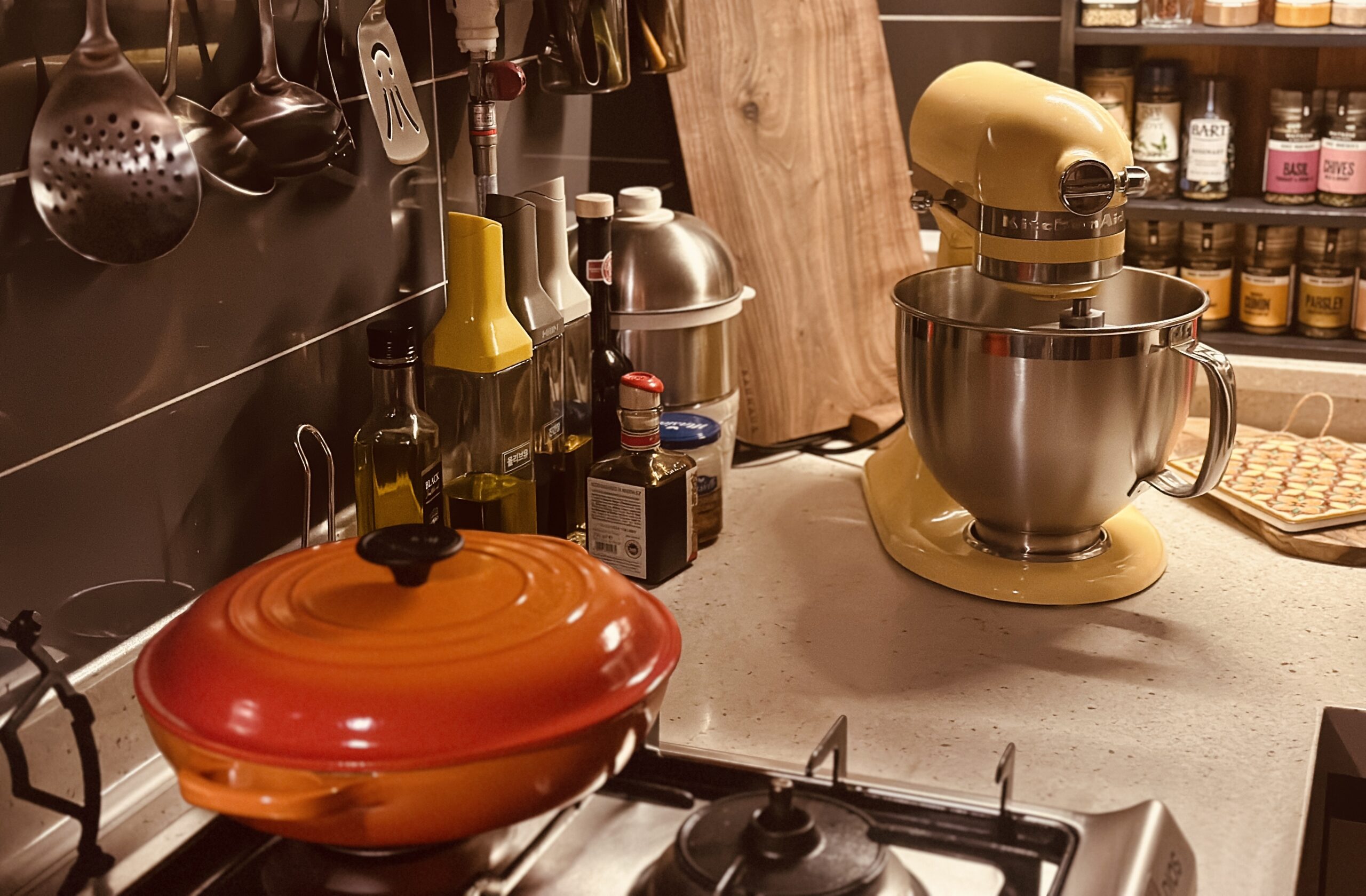 Home kitchen counter with a stand mixer, hanging utensils and an orange Dutch oven on the stovetop