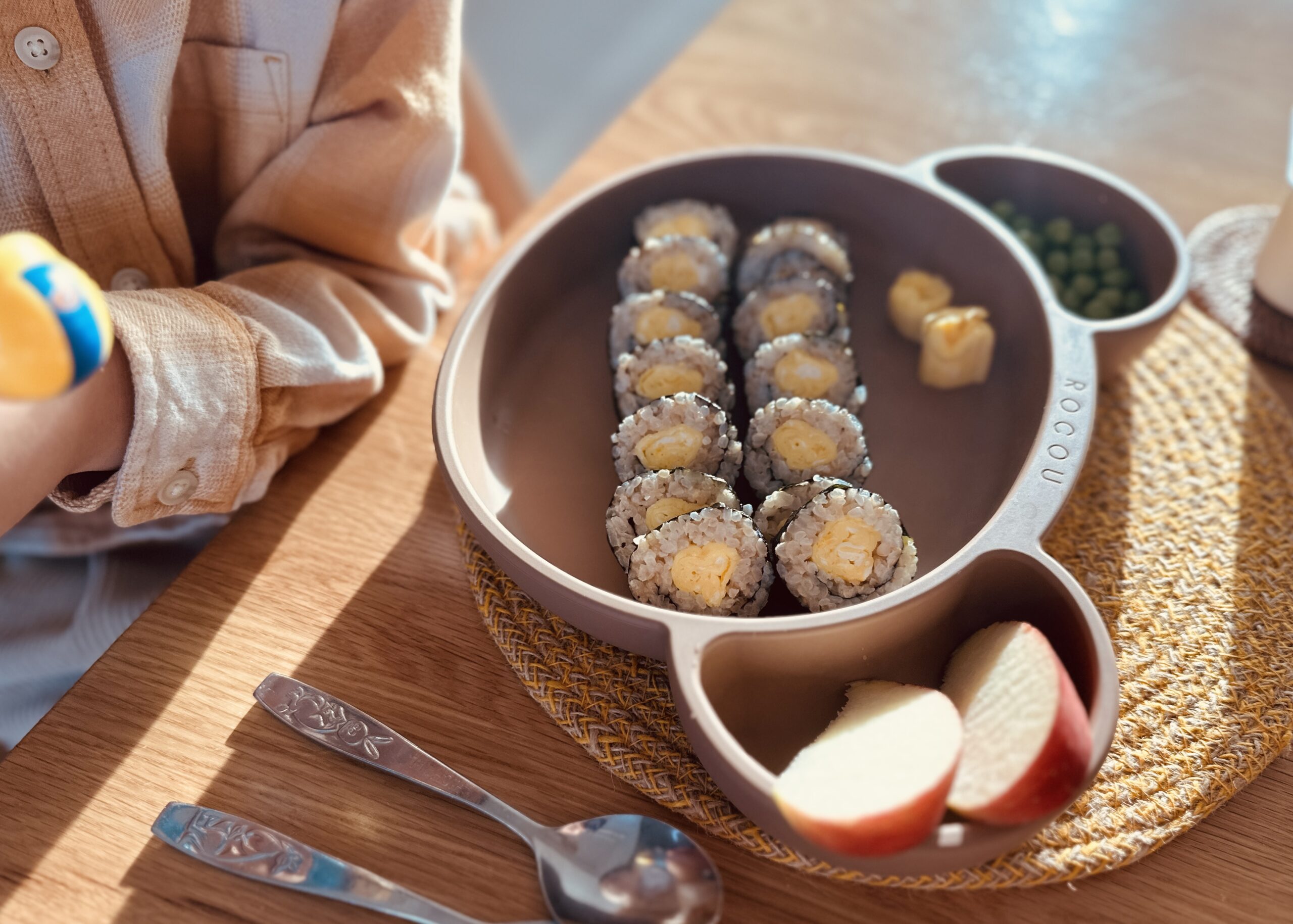 Egg kimbap served on a child’s plate with apples and peas in natural sunlight