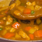 Close-up of mild Korean curry with tender pork, potatoes, carrots, and peas in a thick, glossy sauce