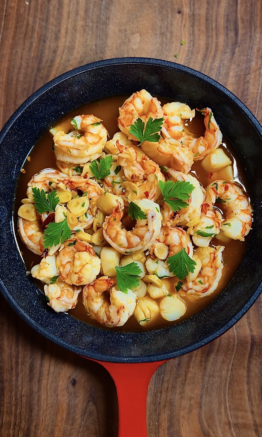 Top view of gambas al ajillo with garlic and parsley in a red skillet
