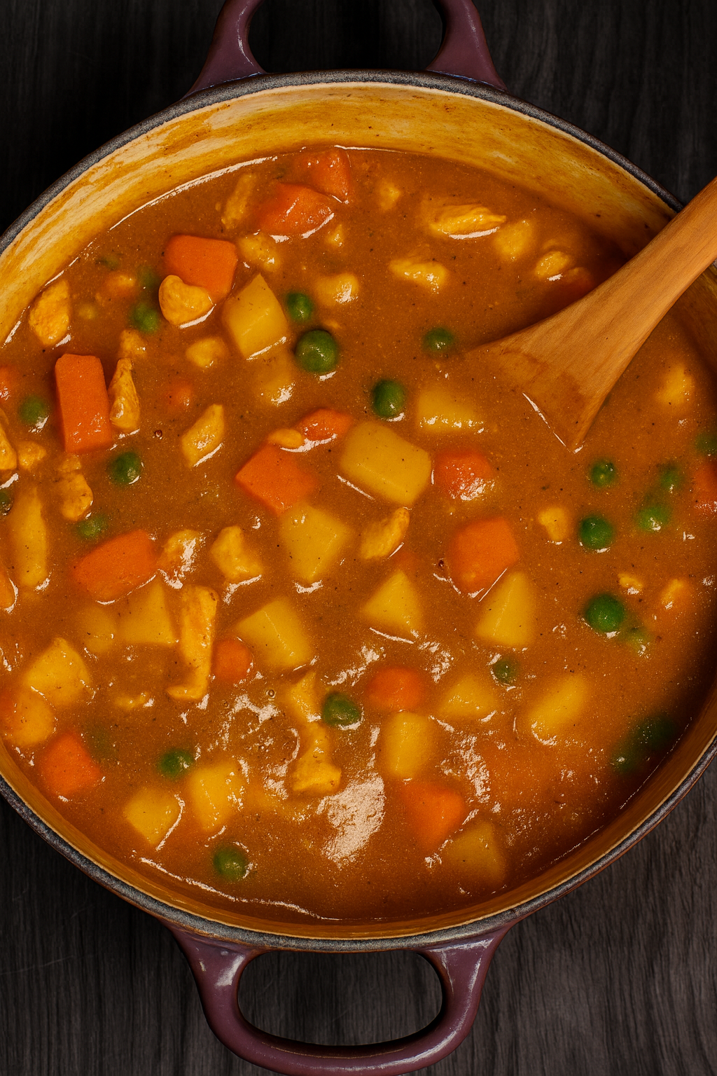 Overhead view of a pot filled with mild Korean curry with potatoes, carrots, peas, and tender pork in a rich golden sauce