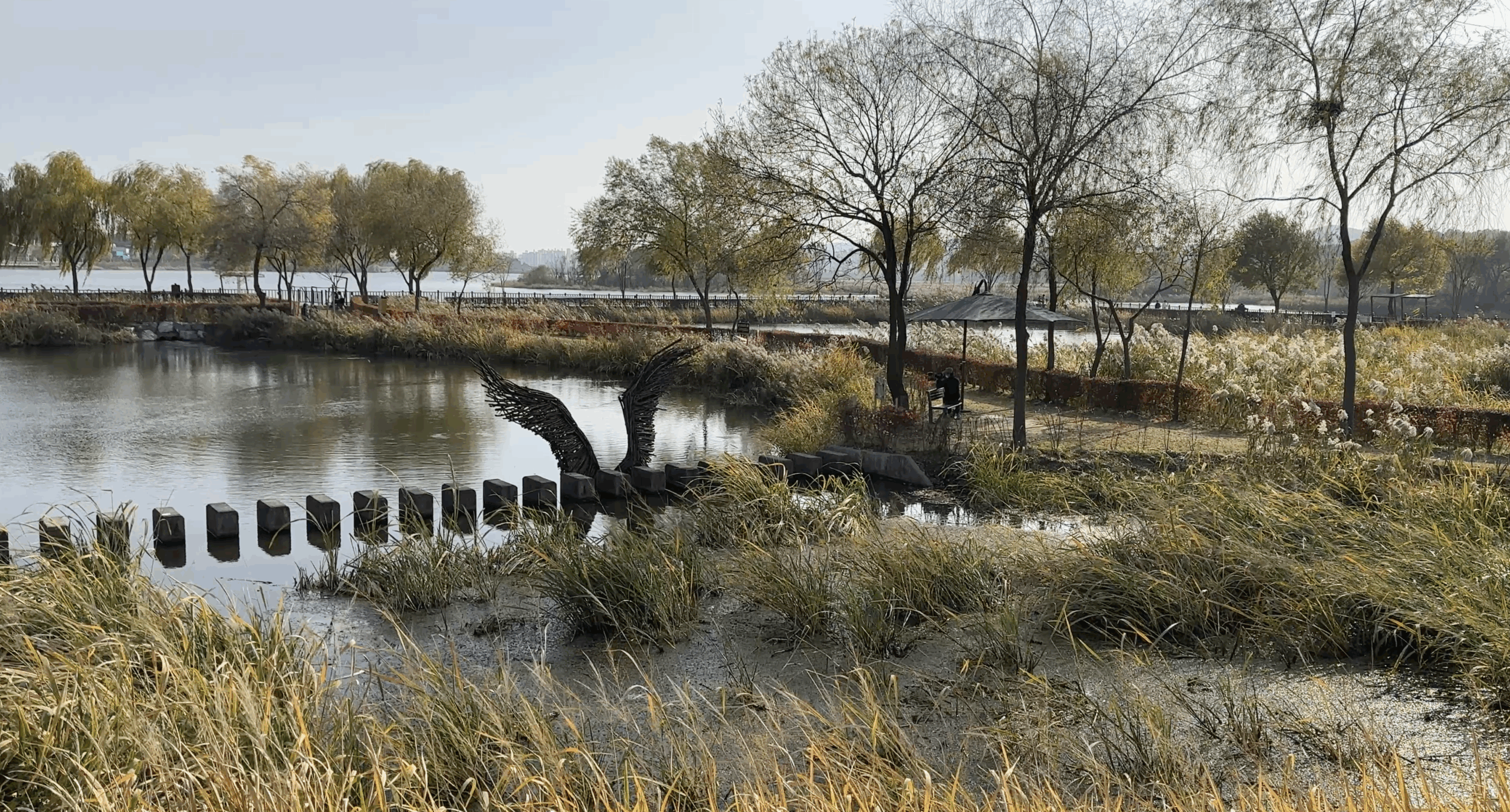 Lakeside landscape with reeds, trees and a large wing-shaped sculpture over the water