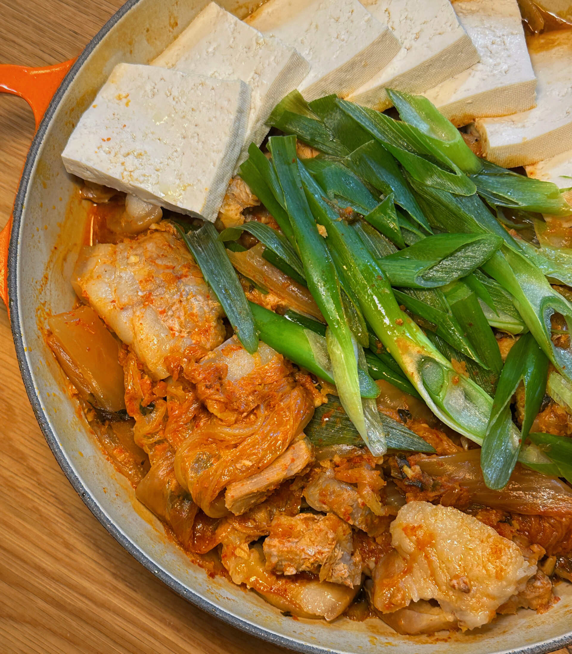 Kimchi-braised pork belly with tofu and green onions arranged in a round dutch oven, ready to serve.