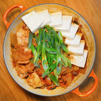 Kimchi-braised pork belly with tofu and green onions arranged in a round dutch oven, ready to serve.