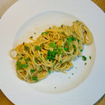 Anchovy lemon butter spaghetti served on a white plate with chopped parsley and black pepper on top