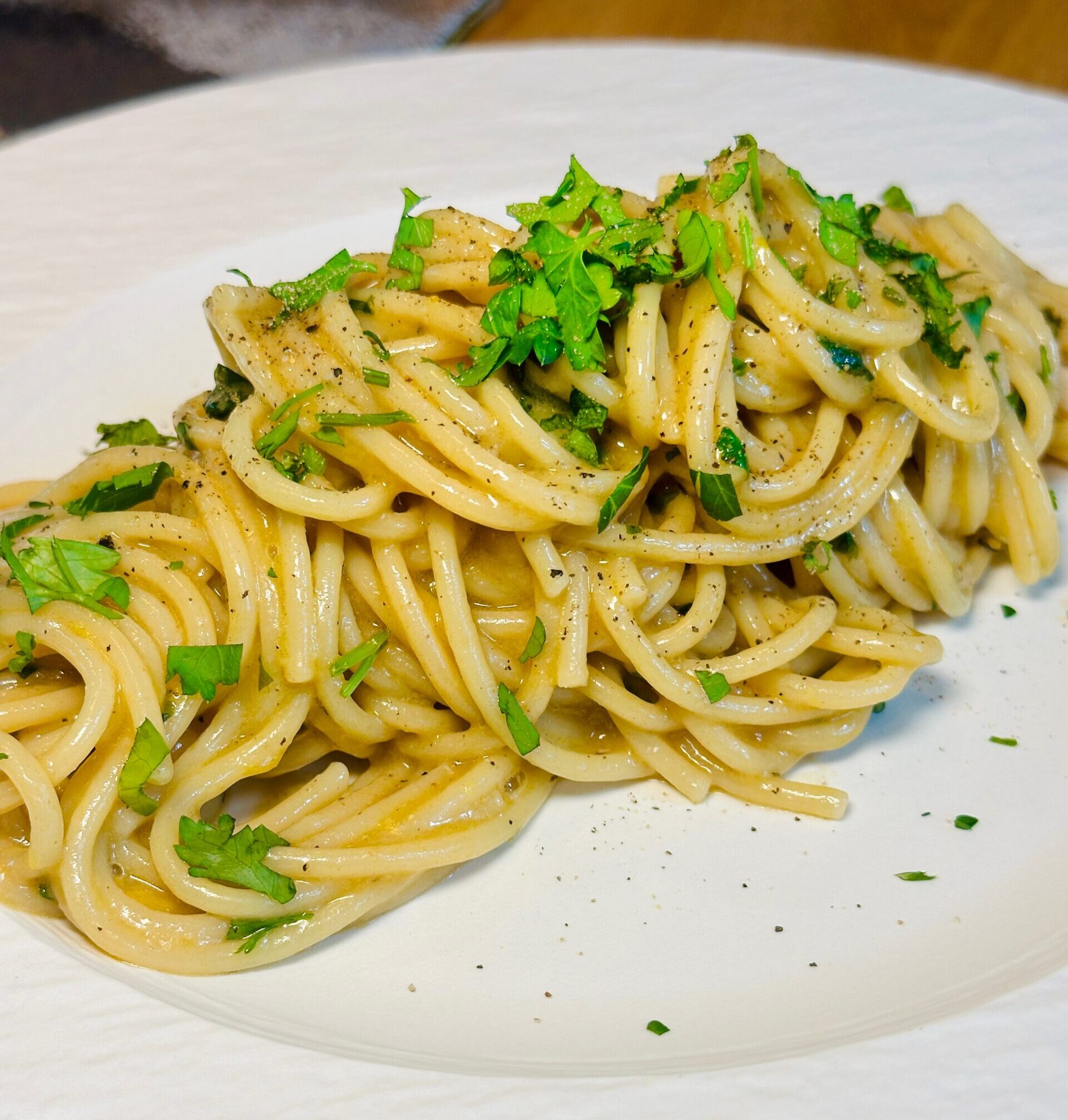 Anchovy lemon butter spaghetti topped with fresh parsley on a white plate