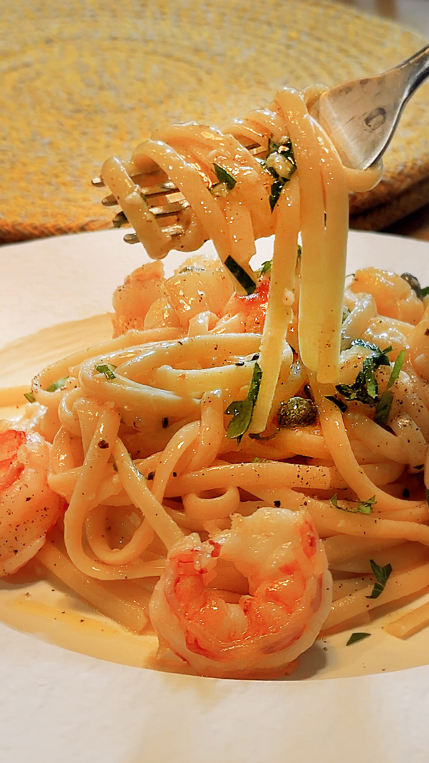 Linguine coated in seafood oil sauce, lifted with a fork, with prawns, parsley and capers visible.