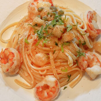 Seafood oil pasta with prawns, scallops, capers and parsley, plated on a white dish.